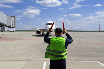 male airport marshal in a yellow uniform helps signals to park by plane. The supervisor meets a...