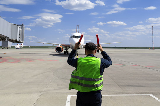 male airport marshal in a yellow uniform helps signals to park by plane. The supervisor meets a passenger plane at the airport. The plane steers into the parking lot.