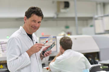 engineer in a factory for the production of electronic components checks the quality of an assembled board with the help of a magnifying glass
