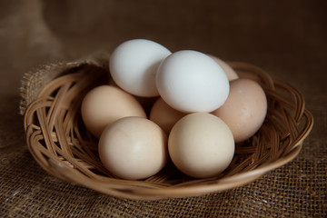 fresh eggs in a wicker basket on a brown background