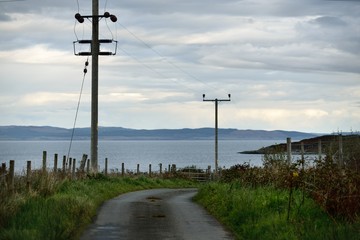 An asphalt road through the lake shore, transformer poles close-up. Hills and mountains in the...