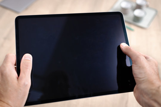Template d'une tablette tenue en main devant une table par un homme travaillant sur un projet artistique, de bureautique ou de projet industriel