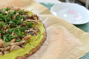 Baked home-made gluten-free pizza from cauliflower and almond flour on baking paper, next to a plate. With avocado sauce, fried chicken, mushrooms and dill. Healthy eating concept. Close-up.