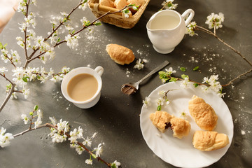 Croissants and coffee with milk on a black background with flowering branches of cherry
