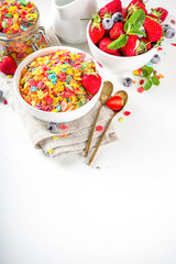 Colorful fruit cereal flakes. Multicolored fruit breakfast corn flakes, with various fruit taste, with milk and fresh berries on white table. Traditional american morning snack