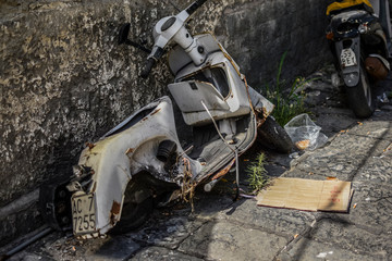 Wreck of white scooter, rusted, damaged, abandoned next to wall. Poor district of Napoli, city full...