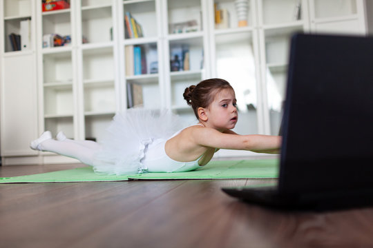 Pretty young ballerina practicing classic choreography during online class in ballet school, online education concept