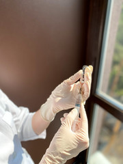 A fair-skinned woman doctor / medical worker in a white coat and disposable gloves holds an open ampoule with a medicine and a syringe in her hands. Free space.