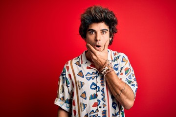 Fototapeta na wymiar Young handsome man on vacation wearing summer shirt over isolated red background Looking fascinated with disbelief, surprise and amazed expression with hands on chin