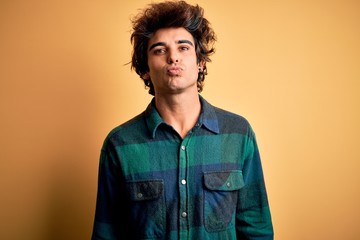 Young handsome man wearing casual shirt standing over isolated yellow background looking at the camera blowing a kiss on air being lovely and sexy. Love expression.