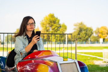 Young girl addictive to a cell phone typing in the amusement park.