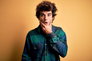 Young handsome man wearing casual shirt standing over isolated yellow background Looking fascinated with disbelief, surprise and amazed expression with hands on chin