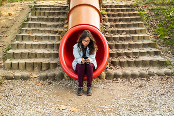 Young girl addictive to a cell phone sitting in slide.