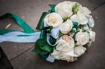 White wedding bouquey of roses and pair of wedding rings on it