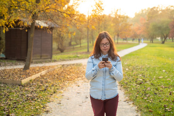 Young girl addictive to a cell phone typing in the middle of the park.