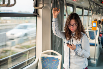 Young girl addictive to a cell phone typing in the tram.
