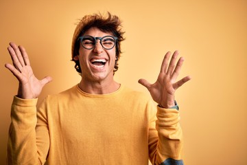 Young handsome man wearing casual t-shirt and glasses over isolated yellow background celebrating...