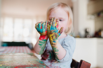 kleines Kind malt zuhause mit bunter Fingerfarbe kleines Mädchen mit farbenfrohen Händen bastelt...