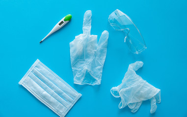 Medical protective mask, rubber gloves, thermometer and protective glasses lie on a blue background with a middle finger in a center. Anti-virus protection kit against covid-19.