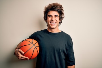 Young handsome sportsman holding basketball ball standing over isolated white background with a happy face standing and smiling with a confident smile showing teeth