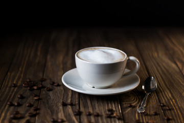 a Cup of coffee with milk and foam, coffee beans on a dark wooden background. selective focus