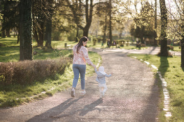 Fototapeta premium Back view of Beautiful mom with adorable daughter walk in the park. Happy family spend time in Mother's Day. Cute little girl with mother. Stylish female run and have fun