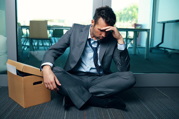 Depressed bankrupt businessman sitting on the floor worried about unemployment