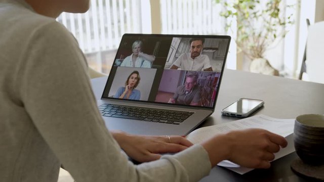 Woman at home listening to the conversation of colleagues and looking at a document during a video conference. Group of business men and women meeting online over a video call to discussing new strate