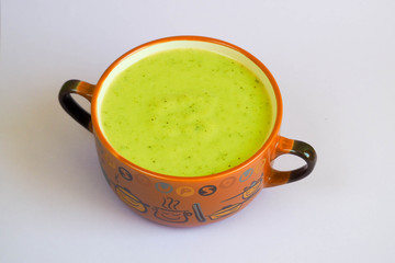 brown deep dish with handles of light green soup mashed broccoli zucchini potatoes onions and cream on a light background . gluten-free food . diet