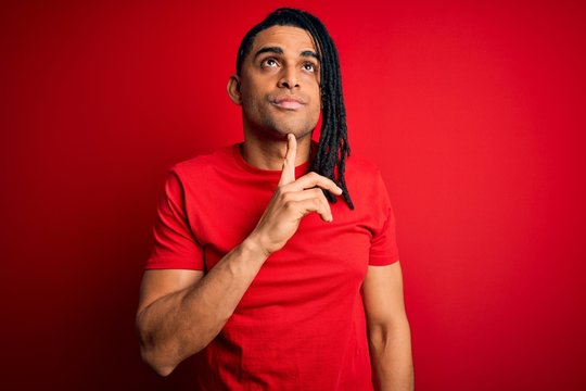 Young handsome african american afro man with dreadlocks wearing red casual t-shirt Thinking concentrated about doubt with finger on chin and looking up wondering