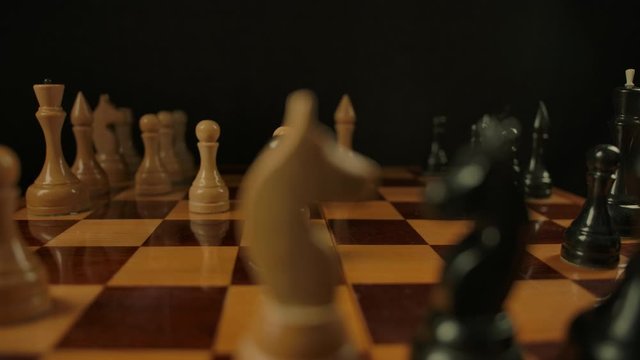 Time lapse of chess game from start to finish, two players moving chess pieces. Smooth dolly movement of macro camera near the wooden chess figures and checkerboard with black background.