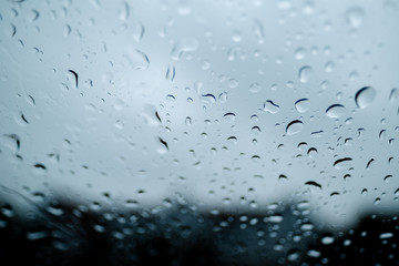 Drops of water running down the windshield of a car. Photo taken from a low angle, so the dark sky can be seen vaguely through the raindrops.