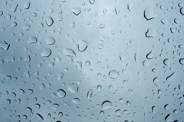 Drops of water running down the windshield of a car. Photo taken from a low angle, so the dark sky can be seen vaguely through the raindrops.