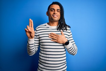 Young handsome african american afro man with dreadlocks wearing casual striped sweater smiling swearing with hand on chest and fingers up, making a loyalty promise oath