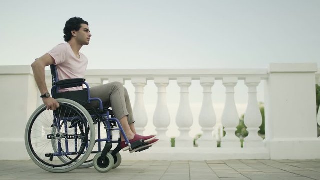 Young man in a wheelchair rides along a path in a public garden.