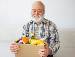 Donation. A senior citizen is holding a cardboard box with food from volunteers. Getting social assistance for the elderly during a pandemic. Close-up. Charity during Covid-19 pandemic.
