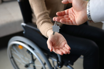 Close-up of realtor putting keys from new apartment on owners hand. Person sitting in wheelchair....