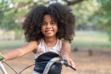 African American girl smiling and looking at camera while riding a bicycle in the park