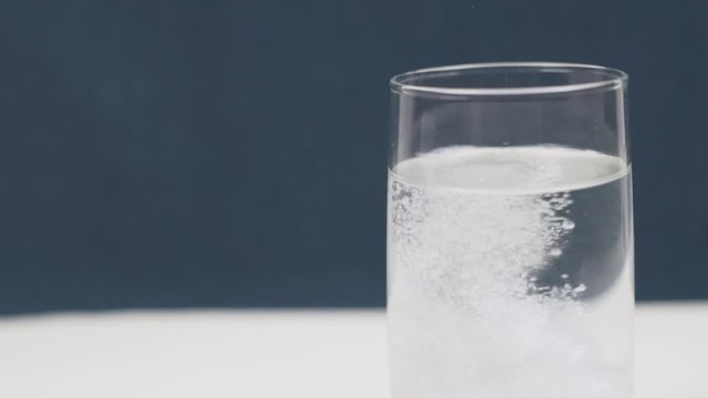 Close up Effervescent Fizzy Tablet Aspirin Paracetamol Vitamin C falls into the Water. Fizzy Pill in a Glass of Water. The tablet Dissolves with the Bubbles.