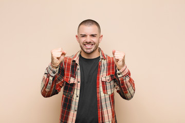 young handsome man feeling happy, positive and successful, celebrating victory, achievements or...