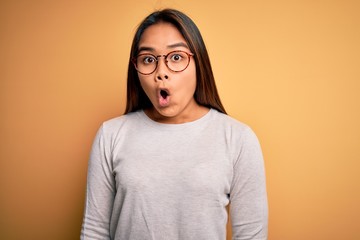 Young beautiful asian girl wearing casual sweater and glasses over yellow background afraid and shocked with surprise expression, fear and excited face.