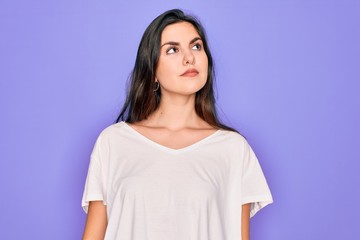 Obraz premium Young beautiful brunette woman wearing casual white t-shirt over purple background smiling looking to the side and staring away thinking.