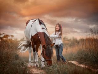 Little girl in indian style with pinto pony in a summer field in sunny evening
