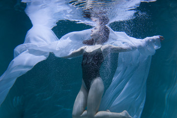 Beautiful girl swims underwater with long hair. Blue or gold background like gold. The atmosphere of a fairy tale or magic. Diving under the water with a shiny cloth