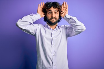 Young handsome business man with beard wearing shirt standing over purple background Doing bunny ears gesture with hands palms looking cynical and skeptical. Easter rabbit concept.