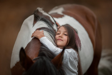 Little girl in indian style with pinto pony in a summer field in sunny evening