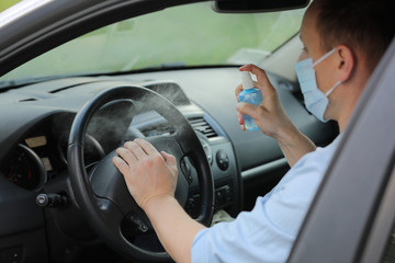 Spraying antibacterial sanitizer spray on steering wheel car, infection control concept. Prevent...
