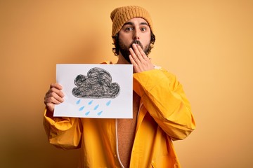 Young handsome man with beard wearing raincoat for rainy day holding banner with cloud cover mouth...