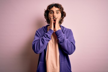 Young handsome sporty man with beard wearing casual sweatshirt over pink background afraid and shocked, surprise and amazed expression with hands on face