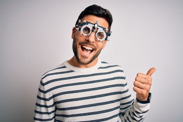 Young handsome man with beard wearing optometry glasses over isolated white background smiling with happy face looking and pointing to the side with thumb up.